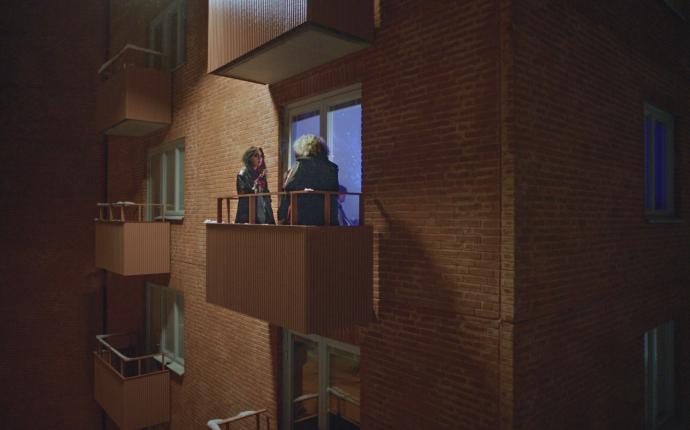 Två kvinnor står på en balkong som tillhör ett flevånings tegelhus.