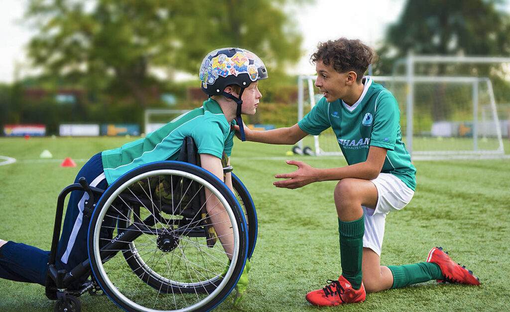 Två killar i fotbollströjor, en hänger över en rullstol.