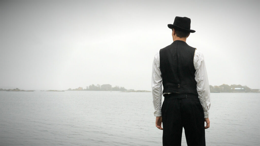 En man med hatt står vid havet, med ryggen mot kameran.