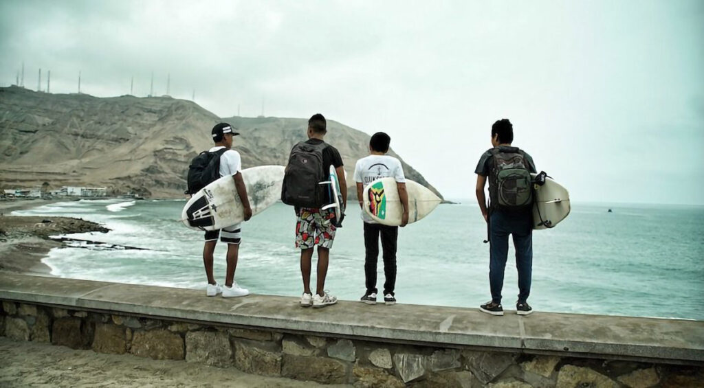 Fyra killar med surfbrädor står mot havet med ryggen till.