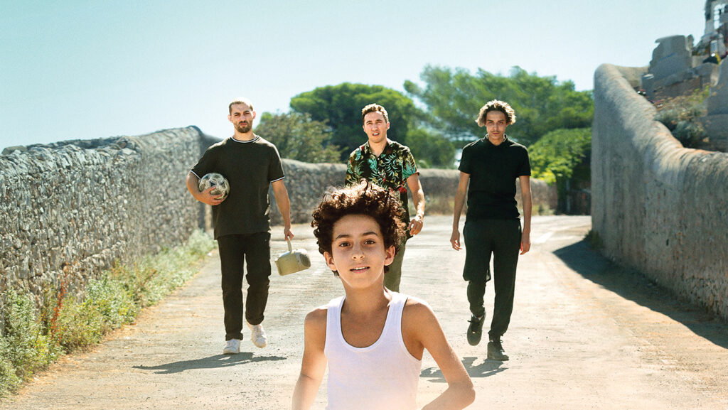 En liten kille springer på en sandig väg med tre äldre killar efter.