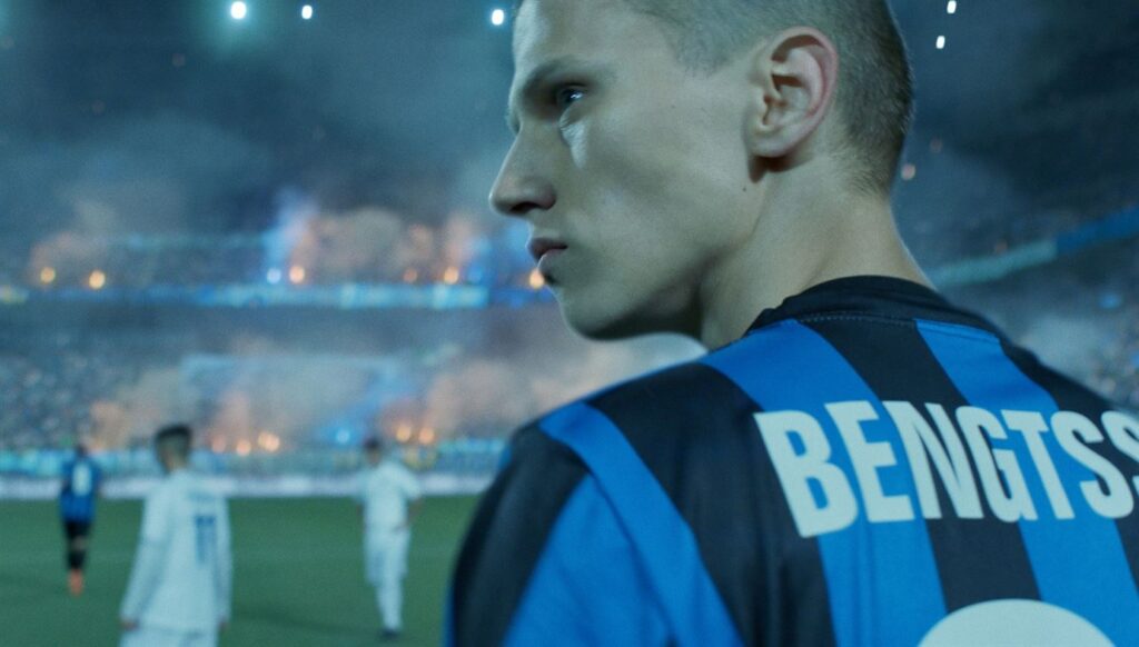 En ung kille i fotbollströja på ett stadion.