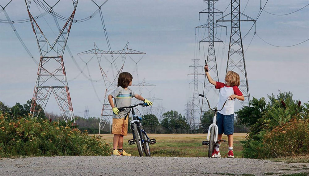 Två killar med cyklar står framför höga elmaster.