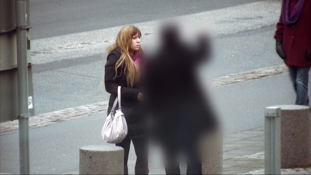 En ung kvinna med handväska pratar med en skugglik mansgestalt.